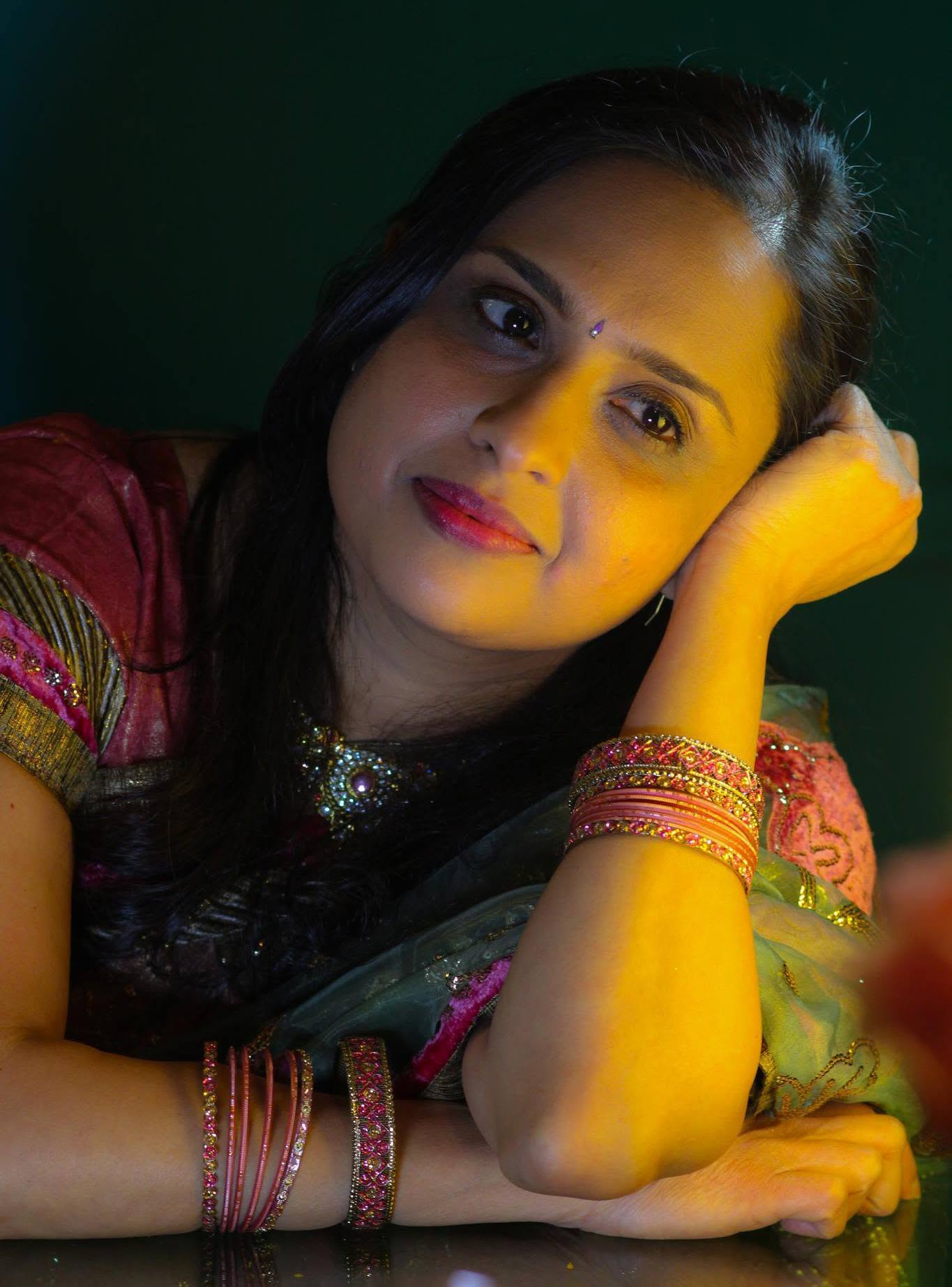 Madhuwanti Bhat in a colourful sari, resting her head on her hand under warm golden light.